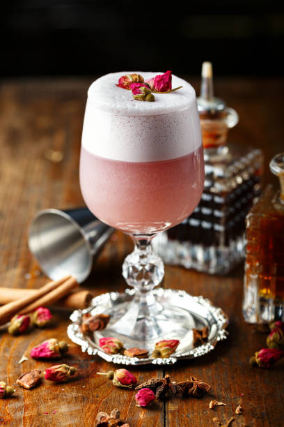 pink cocktail with foam, decorated with pink buds, on the bar. there are spices, a tool for making a cocktail"n